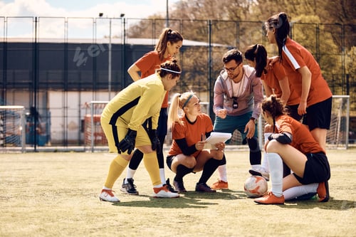 Preview: Soccer coach giving instructions to female players on playing field.