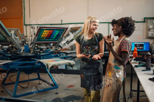 Preview: Interracial female graphic industry workers discussing order on cellphone