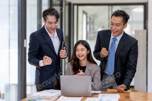 Preview: Business team celebrating success at the office with raised fists.