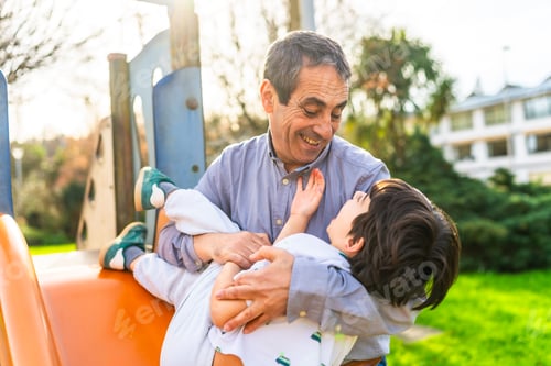 Preview: Grandfather holding grandson lovingly at playground on sunny day