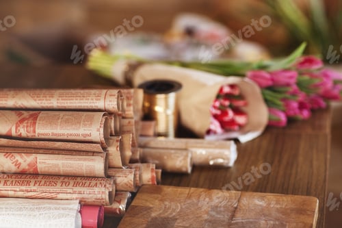 Preview: On a wooden table lies craft paper wrapping tape and pink tulips.