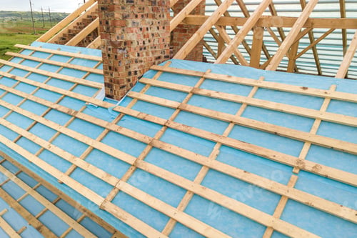 Preview: Aerial view of a brick house with wooden roof frame under construction.