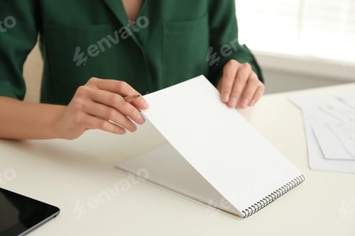 Preview: Woman with pencil and notepad at white table, closeup
