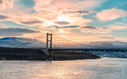 Preview: Sunset over suspension bridge on Jokulsarlon glacial river lagoon with iceberg floating at Iceland