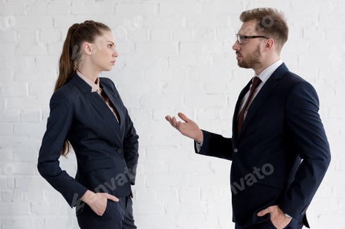 Preview: serious businessman and businesswoman in suits discussing near white wall