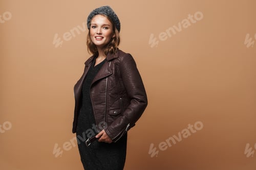 Preview: Young pretty smiling woman in hat, leather jacket and black dress dreamily looking in camera