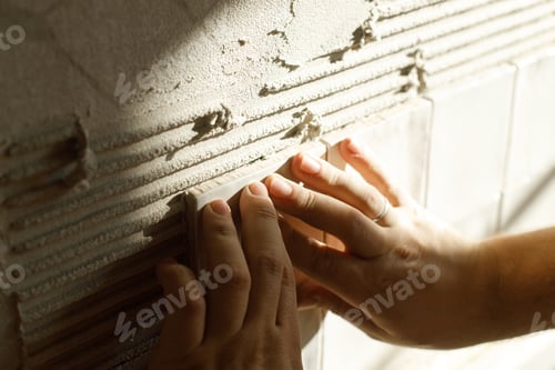 Preview: Hands laying modern square tile on adhesive close up