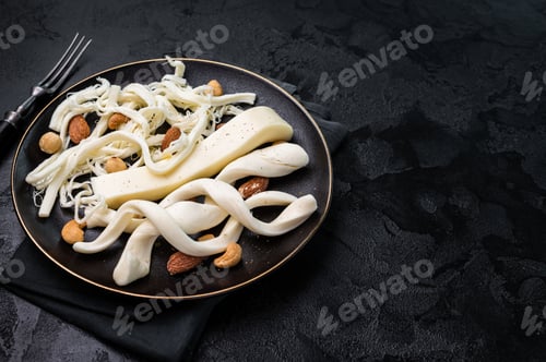 Preview: Smoked Traditional Chechil white cheese on a plate with nuts, black background.