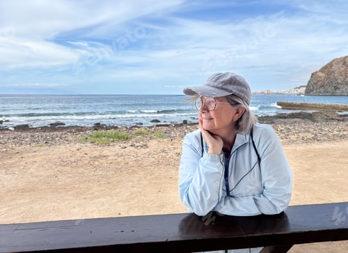 Preview: Attractive senior gray-haired woman at the beach looking away enjoys freedom and retirement