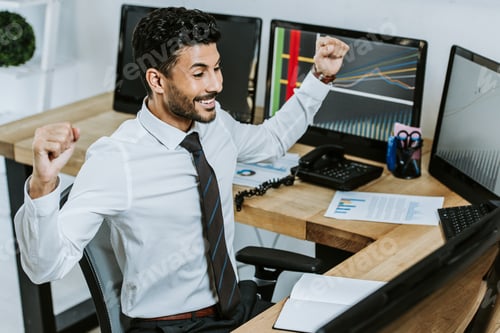 Preview: high angle view of smiling bi-racial trader looking at computer and showing yes gesture