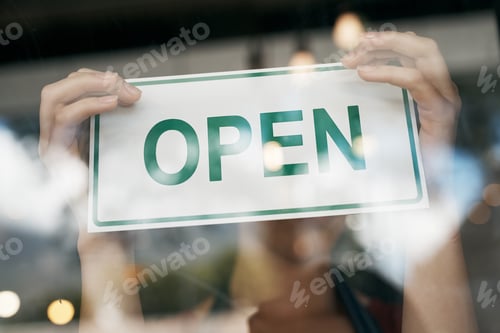Preview: Cropped shot of a woman hanging an open sign on the door of her store