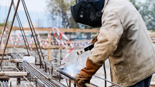 Preview: A worker at construction site is welding iron pipe with electrode in a protective uniform