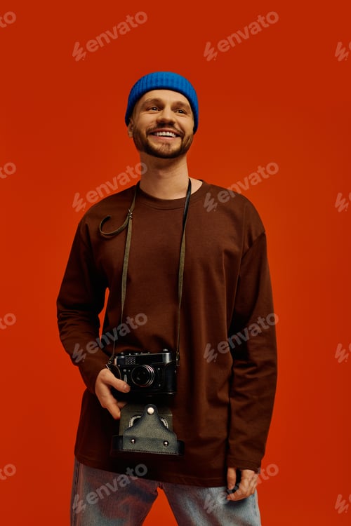 Preview: Captivating young man smiles confidently while holding a camera in a vibrant background