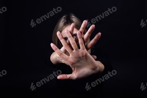 Preview: Female person with hands in front of her showing stop sign hiding face in black dress on black