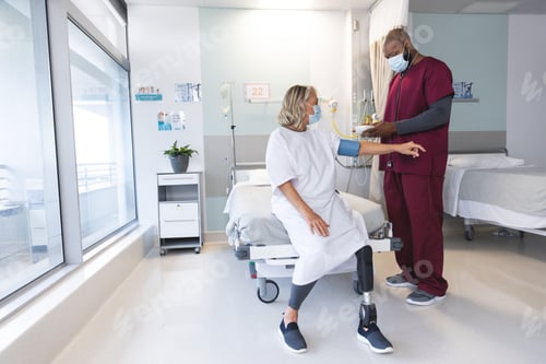 Preview: African american doctor measuring blood pressure of senior caucasian patient with prosthetic leg