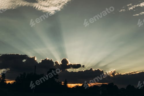 Preview: dramatic amazing sun and sunset light rays through clouds in sky in summer