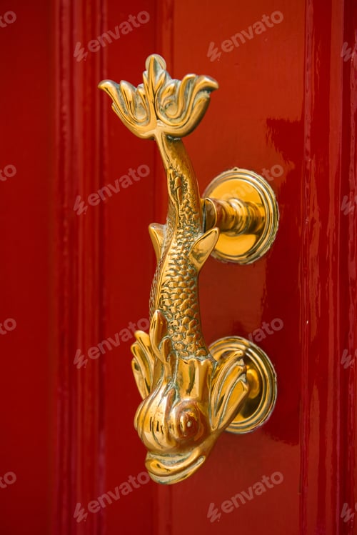 Preview: Close-up view of the fish shaped golden knocker on a red wooden door. Valetta, Malta