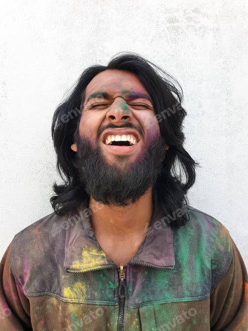 Preview: Closeup of good looking young man covered with multi color holi powder with white wall background