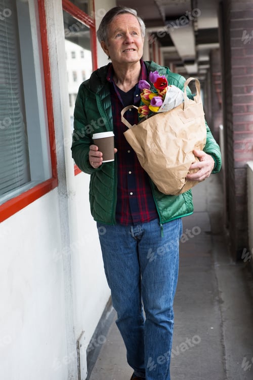 Preview: Man holding flowers and a coffee cup leaning against a building.
