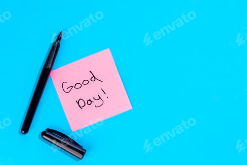 Preview: Pink note with inscription Good day and marker on blue background, flat lay.