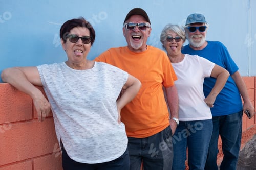 Preview: Group of happy senior friends enjoy time together outdoors, leaning against a colorful wall