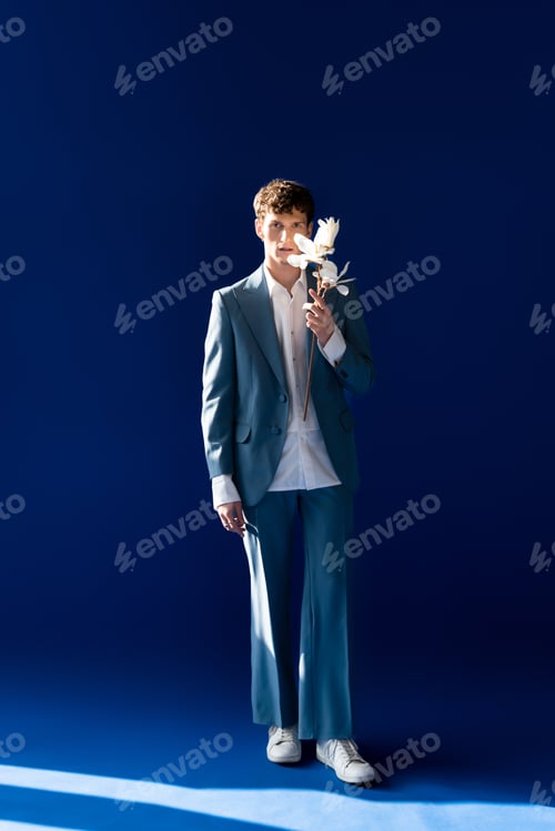 Preview: Full length of trendy young model holding magnolia branch on navy blue background