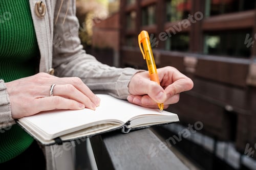 Preview: Woman writing notes outdoors with an orange pen
