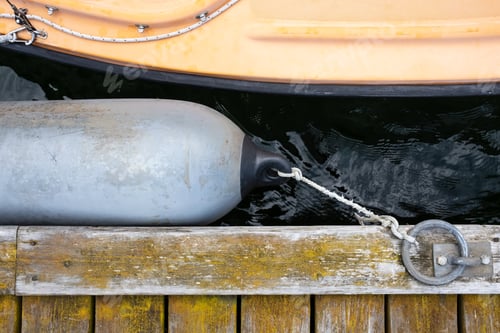 Preview: Marine fender tied with a rope to a metal ring on an old weathered pier protects boat from damage
