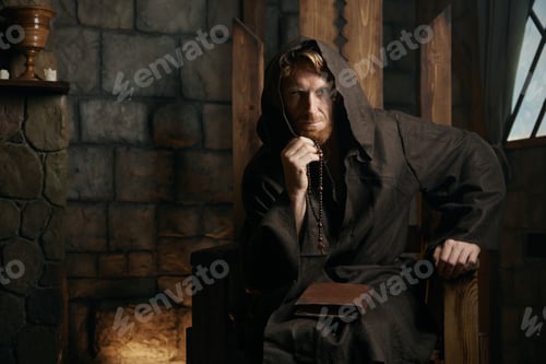 Preview: Portrait of medieval monk in hood sitting on wooden armchair