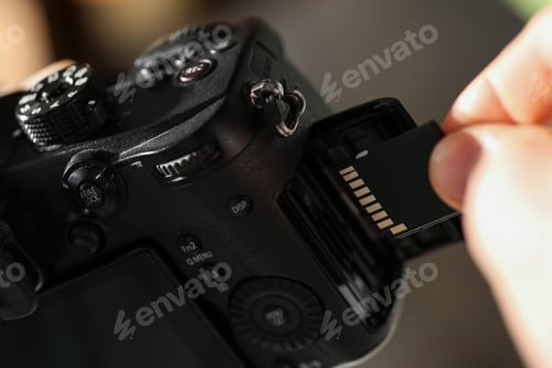 Preview: Man inserting SD memory card into photo camera indoors, closeup