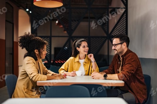 Preview: Colleagues having fun during the coffee break at the workplace, sitting at the table.