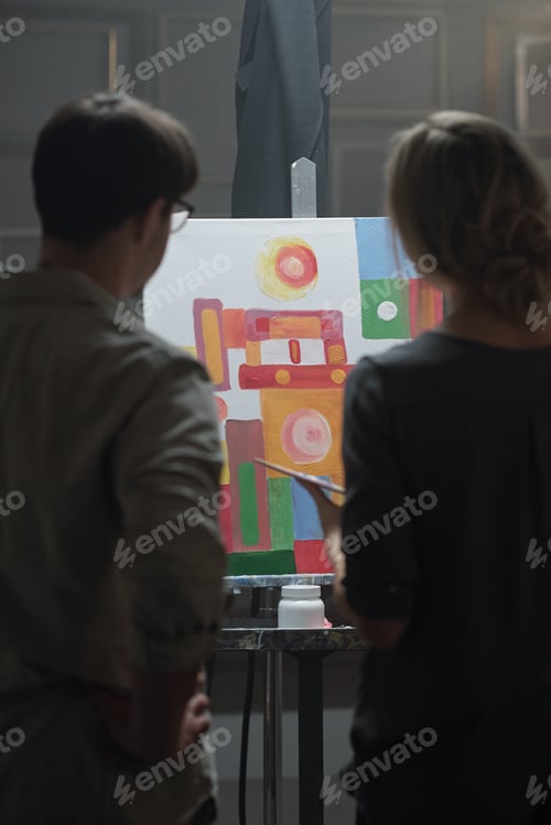 Preview: Young female student of art school and her teacher standing in front of easel