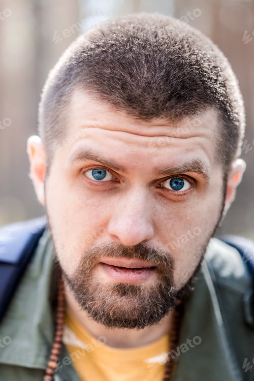 Preview: a young man with a short haircut and blue eyes in a green jacket - the face of a millennial close-up