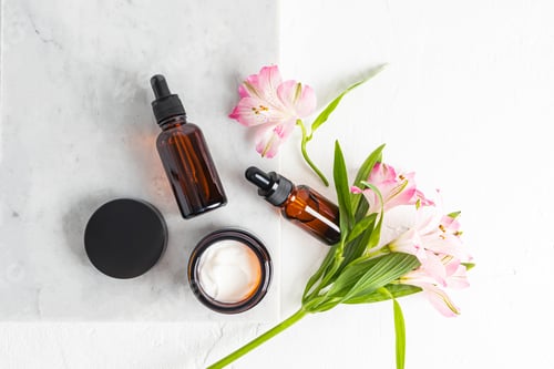 Preview: Cosmetic set of glass bottles with pipette and open jar of face care cream on white marble podium