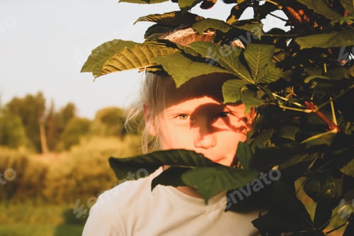 Preview: A little blonde girl behind the chestnut tree. Happy childhood. Summer vacations in the countryside.