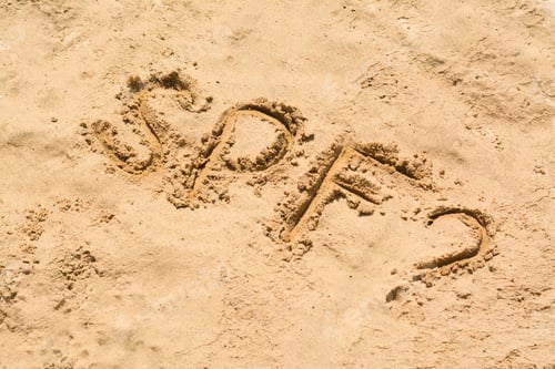 Preview: Abbreviation SPF and question mark written on sand at beach, above view