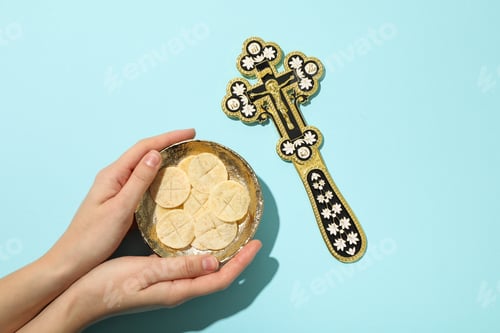 Preview: Bread in bowl in hands and cross on blue background, top view