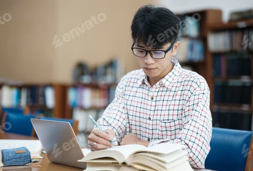 Preview: Young Asian male sitting inside a library alone doing research.