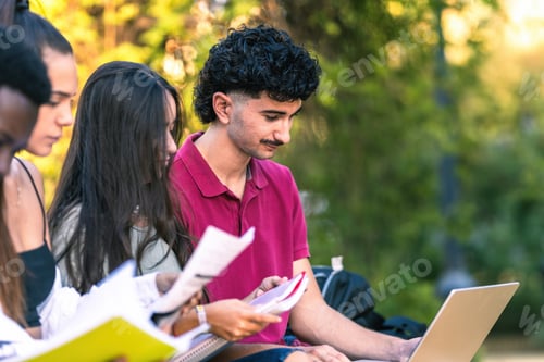 Preview: Diverse young people studying with laptop and papers sitting on a bench outdoors