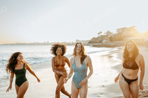 Preview: Summertime fun. Group of carefree women friends laughing while running in swimwear at the beach