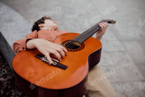 Preview: child lying on his back, playing guitar, dressed in a shirt,