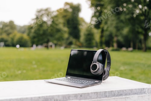 Preview: Laptop and headphones on a wall in a park