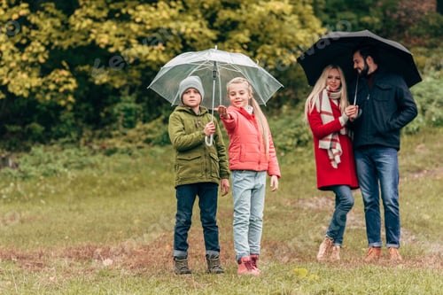 Preview: adorable little kids and young parents holding umbrellas in autumn park