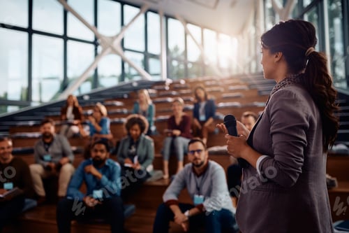 Preview: Female business leader talking to group of seminar attendees at convention center.