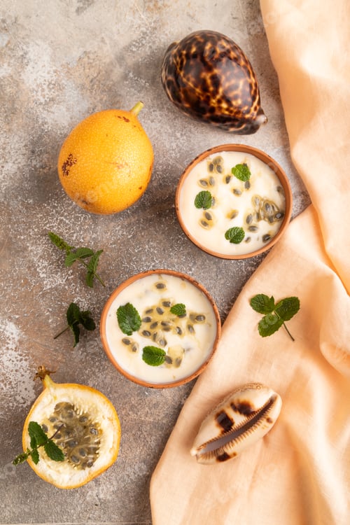 Preview: Yoghurt with granadilla and mint in clay bowl on brown concrete, top view.