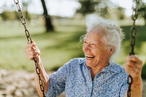 Preview: Cheerful senior woman on a swing at a playground
