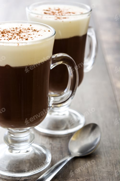 Preview: Two glasses of hot chocolate with whipped cream and cinnamon sprinkles are sitting on a table