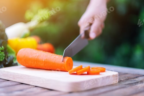 Preview: Closeup image of a woman cutting and chopping carrot by knife on wooden board