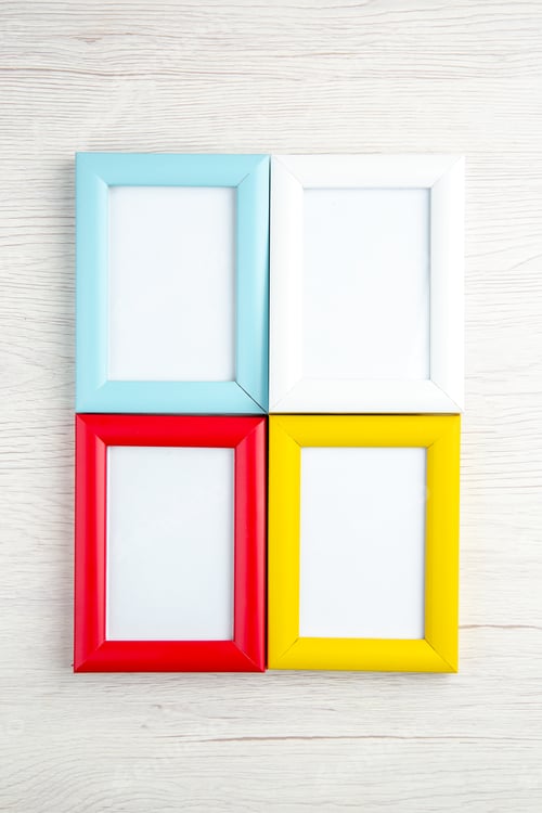 Preview: Overhead view of four empty picture frames in different colours on stripped background
