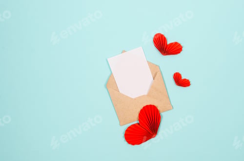 Preview: Empty white paper blank in craft envelope and varios paper hearts on blue background.